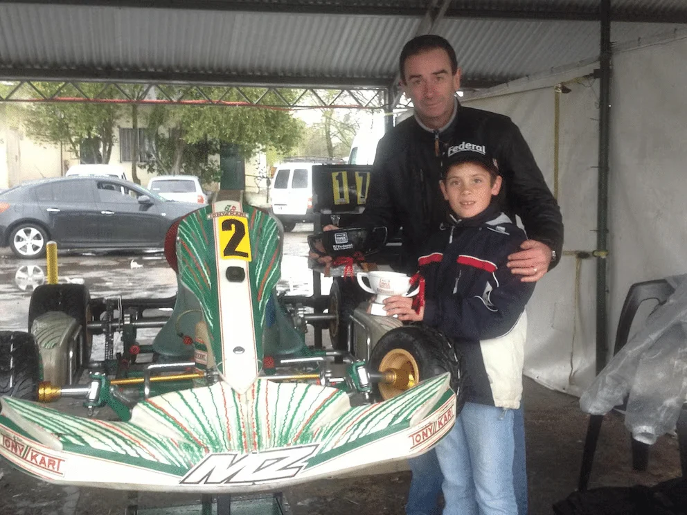 Franco de chico con un trofeo junto a su papá y su kart.